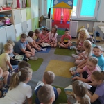 Uczniowie siedzą na dywanie, nauczyciel stoi na środku sali.