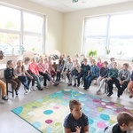 Grupa uczniów siedzi na krzesełkach wokół kolorowego dywanu..jpg