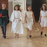 Grupa dziewczynek przebranych za bogów greckich idzie korytarzem szkolnym.jpg
