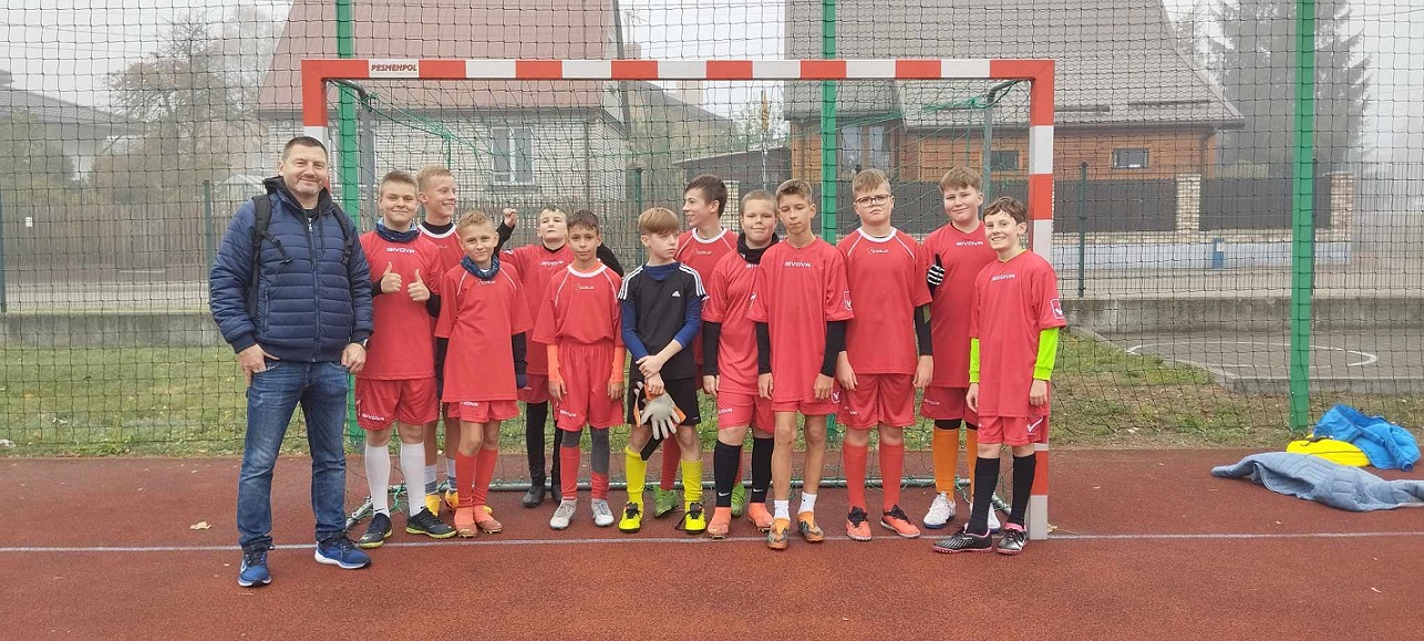 Grupa uczniów ubrana w czerwone sportowe stroje stoi przy bramce piłkarskiej..jpg