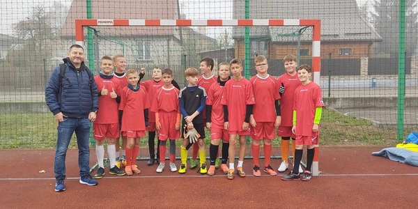 Grupa uczniów ubrana w czerwone sportowe stroje stoi przy bramce piłkarskiej..jpg