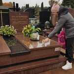Uczennica zapala znicz przy pomniku z kwiatami na cmentarzu..jpg