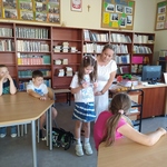 Uczniowie siedzą przy stolikach, na środku stoi naczyciel z uczniem.