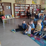 Pisarka rozmawia z uczniami_ którzy siedzą na kolorowym dywanie  w bibliotece..jpg