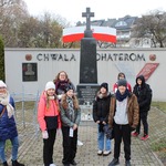Grupa osób ubrana ciepło stoi przy pomniku poświęconym bohaterom..jpg