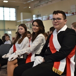 Troje uczniów ubranycn na galowo, przepasani biało-czerwonymi szarfami.