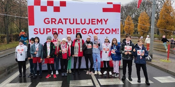 Grupa uczniów ubranych w barwy biało-czerwone stoi na podium z medalami w rękach..jpeg