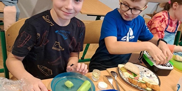 Dwóch chłopców przygotowuje kanapki przy stole z produktami spożywczymi..jpg