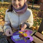 Dziewczynka stoi przy ławie i trzyma w ręku paletę z kompozycją liści..jpg