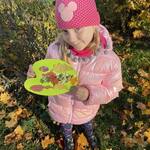 Dziewczynka stoi wśród kolorowych liści i trzyma w ręku paletę z kompozycją liści..jpg