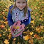 Dziewczynka wstoi wśród kolorowych liści i trzyma w ręku paletę z kompozycją z kwiatów..jpg