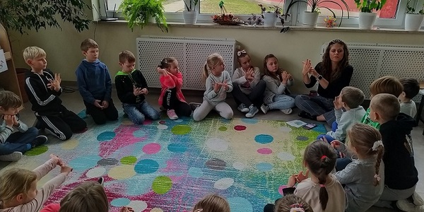 Uczniowie siedzą wokół dywanu i uczą się wyciszać emocje za pomocą oddechu obserwując nauczyciela..jpg