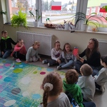 Nauczyciel pokazuje dzieciom siedzącym wokół dywanu słoik z różowym płynem i brokatem.jpg