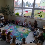 Uczniowie siedzą wokół kolorowego dywanu i słuchają nauczyciela..jpg