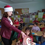 Nauczycielka w czapce Mikołaja rozdaje uczniom książki.jpg