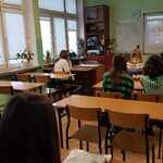 Uczeniowie siedzą w klasie oglądają lekcję online na ekranie..jpg