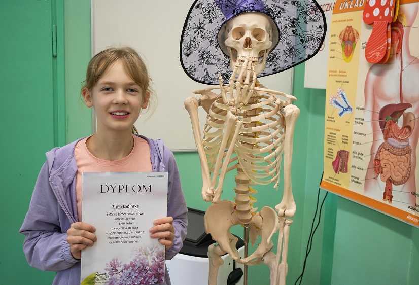 Uczennica stoi obok modelu szkieletu człowieka.