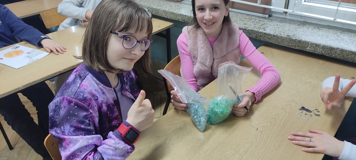 Dwie uczennice pokazują foliowe torebki z zielonym tworzywem..jpg