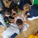 Czworo uczniów pochyla się nad kartkami na korytarzu szkolnym..jpg