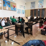 Dziewczyny rzucaja kulami papierowymi zza krzesł w sali szkolnej.jpg