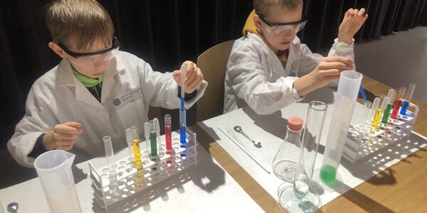Dwóch uczniów w fartuchach wykonuje eksperyment chemiczny..jpg