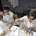 Dwóch uczniów w fartuchach wykonuje eksperyment chemiczny.jpg