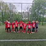 Chłopcy ubrani w sportowe czerwone koszulki odwróceni w stronę bramki na boisku.jpg