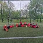 Grupa chłopców ubranych w czerwone stroje sportowe lezy na zielonej murawie..jpg