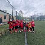 Grupa chłopców ubranych w czerwone stroje sportowe stoi na boisku szkolnym..jpg