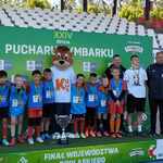 Chłopcy w sportowych strojach  i z medalami na szyjach stoją na podium.jpg