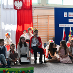 Chłopiec przebrany za króla siedzi razem z innymi dziećmi na sali gimnastycznej, w tle tablica z czerwonymi makami oraz flaga polski