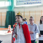 Chłopiec przebrany za króla wchodzi na salę gimnastyczną, w tle tablica z czerwonymi makami oraz flaga polski