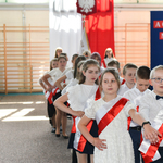 Dzieci z szarfami biało-czerownymi tańczą na sali gimnastycznej.