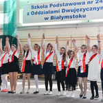 Dzieci z szarfami biało-czerownymi tańczą na sali gimnastycznej.