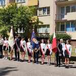 Grupa uczniów ubranych w stroje galowe stoi z pocztami sztandarowymi..jpg