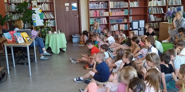 Pisarka czyta w bbliotece uczniom siedzącym na dywanie  fragment swojej książki.jpg