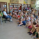 Uczniowie w bibliotece sidzą na dywanie i słuchają pisarki..jpg
