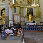 Uczniowie siedzą w ławkach kościoła przed barokowym ołtarzem.