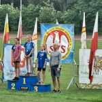 Trzy uczennice stoją na sportowym podium_ obok nich trener_ w tle banery sponsorów..jpg