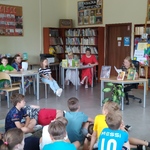 Uczennica czyta książkę przy stoliku_ na przeciw niej siedzą inne dzieci na podłodze_.jpg