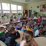 Uczniowie siedzą na podłodze i krzesłach w bibliotece..jpg