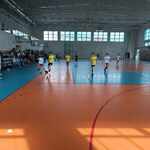 Grupa uczniów gra w piłkę nożną na sali sportowej. Obok stoją kibice..jpg