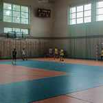 Grupa uczniów gra w piłkę nożną na sali sportowej. W tle elektroniczny zegar.jpg