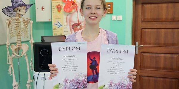 Uczennica trzyma dwa dyplomy w rękach