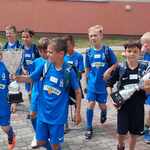 Grupa uczniów ubrana w niebieskie stroje sportowe idzie z pucharami w rękach..jpg