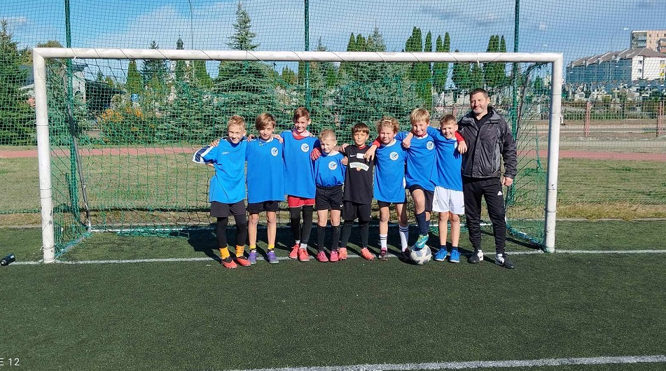 Grupa chłopców ubranych na sportowo wraz z trenere pozuje w bramce do piłki nożnej..jpg