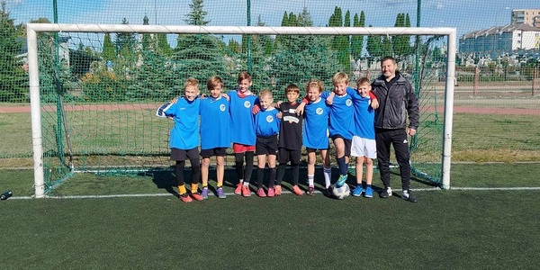 Grupa chłopców ubranych na sportowo wraz z trenere pozuje w bramce do piłki nożnej..jpg