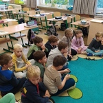 Grupa dzieci siedzi w klasie na niebieskim dywanie..jpg