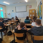 Nauczycielka czyta książkę uczniom siedzącym w ławkach szkolnych..jpg