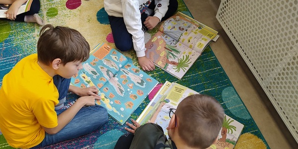Uczniowie czytają ksiązki siedząc n kolorowym dywanie..jpg